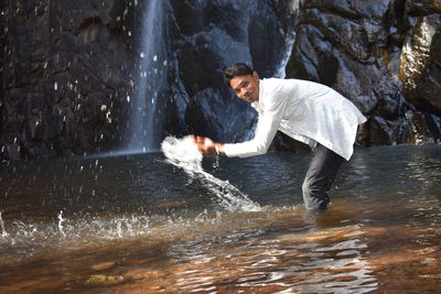 Full length of young man splashing water in rock