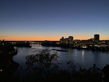 River by illuminated buildings against clear sky at sunset