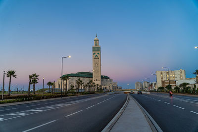 Road leading towards buildings against clear sky