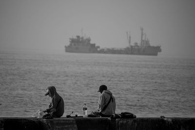 Rear view of men sitting on sea against sky