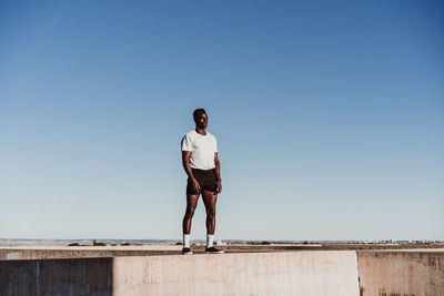 Male athlete standing on wall against blue sky during sunny day