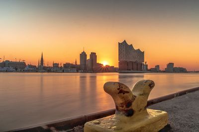 River by buildings against sky during sunset in city