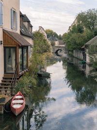 Reflection of house and trees on canal by building against sky