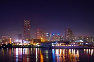 Sea by modern city skyline against clear sky at night