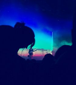 Silhouette people at music concert against blue sky at night