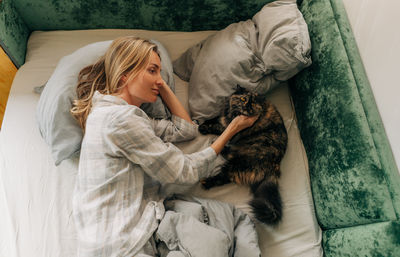 Woman petting cat lying in bed after waking up.