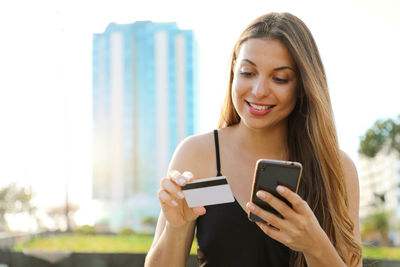 Young woman holding credit card while using smart phone