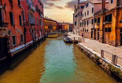 Canal amidst buildings against sky during sunset