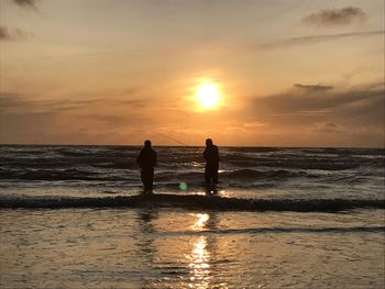 Silhouette people standing on beach against sky during sunset