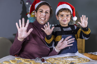 Portrait of smiling mother and son showing messy hands while sitting by table at home