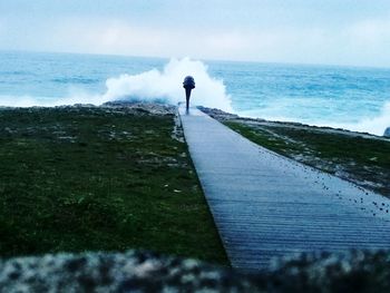 Empty footpath leading towards waves splashing in sea