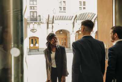 Smiling businesswoman talking with male and female colleagues at doorway of hotel