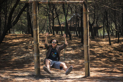 Young man sitting on rope swing in forest