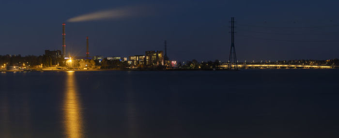 Illuminated city by river against sky at night