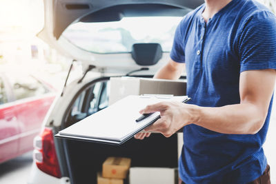 Midsection of man holding clipboard against car