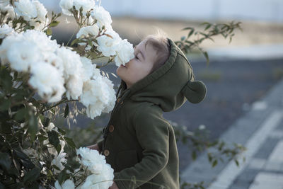 Cheerful toddler girl smelling white roses in the rose garden