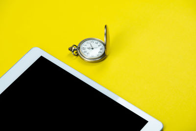 Close-up of clock on table against yellow wall