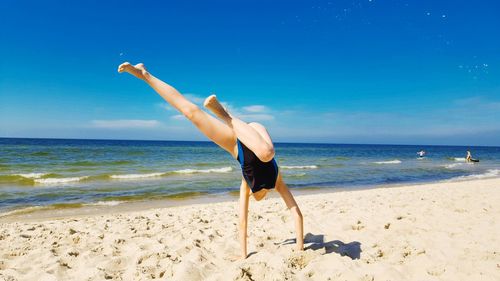 Girl doing handstand at beach against sky