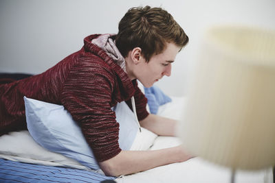 Side view of teenage boy lying on bed at home