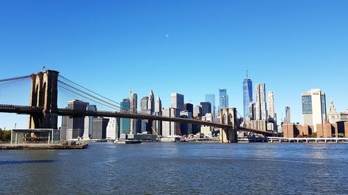 Bridge over river by buildings against clear sky - brooklyn bridge from empire fulton ferry park