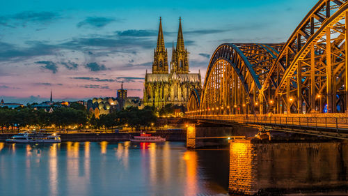 Illuminated bridge over river at sunset