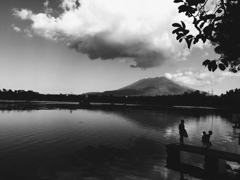 Silhouette people by lake against sky