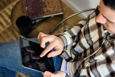 Young man seated at home using digital tablet. chilling next to the window consuming digital content. top view.