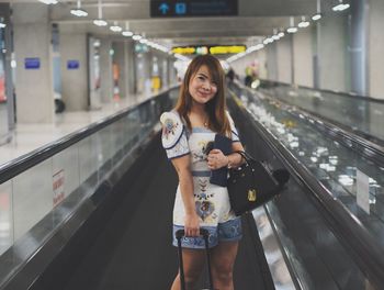 Portrait of smiling woman standing on moving walkway