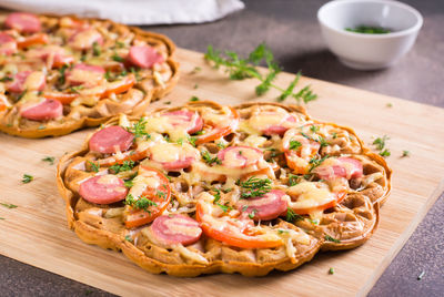 Waffle pizza with tomatoes, sausages, cheese and herbs on a wooden board