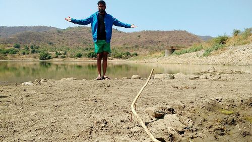 Full length of man standing at lakeshore against mountains