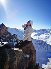 Woman sitting on rock at snowcapped mountain against clear blue sky