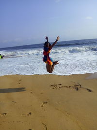 Woman jumping at beach against sky