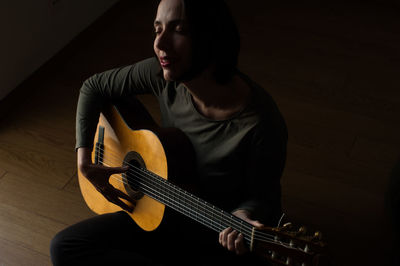 High angle view of woman with eyes closed playing guitar while sitting at home