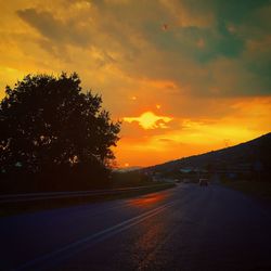 Road by trees against sky during sunset