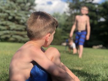 Shirtless boys on grass against trees