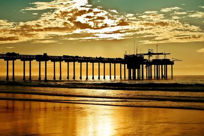 Silhouette built structure on beach against sky during sunset