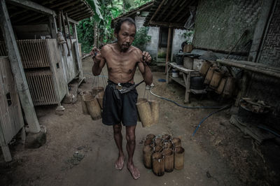 Shirtless man carrying wooden containers while walking amidst cottages