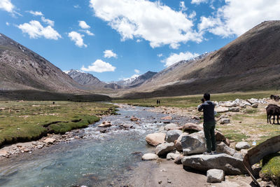 Rear view of man photographing while standing on rocks by mountains against sky