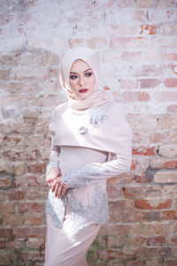 Portrait of beautiful young woman standing against brick wall