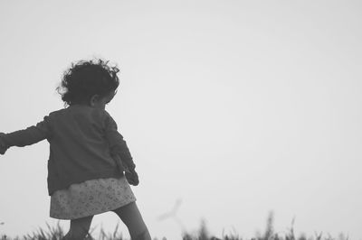 Rear view of girl standing on field against clear sky