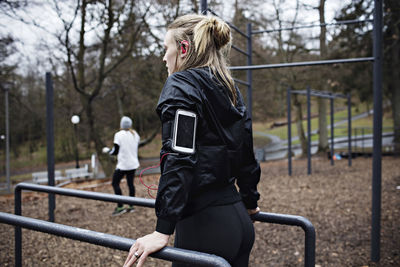 Rear view of female athlete wearing arm band while exercising on parallel bars in forest