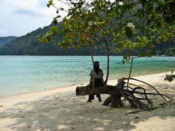 Rear view of woman sitting on driftwood at beach