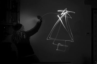 Silhouette person standing by illuminated lighting equipment at night