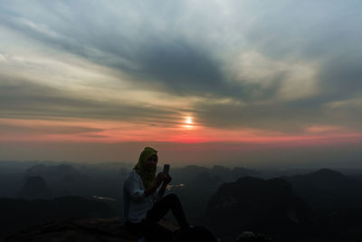 Woman photographing on mountain against sky during sunset