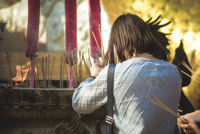 Rear view of woman holding incense while praying in temple