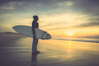 Silhouette man standing on beach against sky during sunset