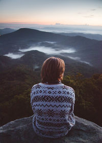 Rear view of woman sitting on mountain during sunset