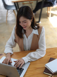 Smiling young businesswoman using laptop while sitting at cafe