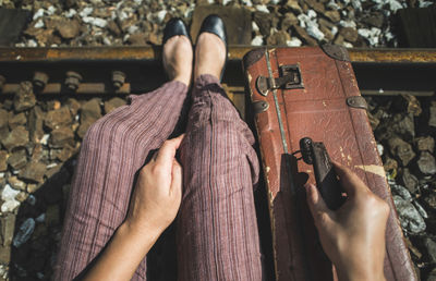 Low section of woman with suitcase sitting on railroad track