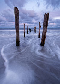 Wooden posts on sea against sky